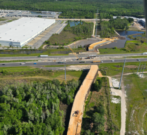 Vista aérea del paso elevado para fauna silvestre en construcción junto a la Interestatal 4 en el condado de Polk, Florida, en la que se aprecian grúas, maquinaria de construcción y terraplenes que se están levantando sobre la autopista, con el tráfico circulando por debajo y humedales y espacios verdes abiertos rodeando la obra.